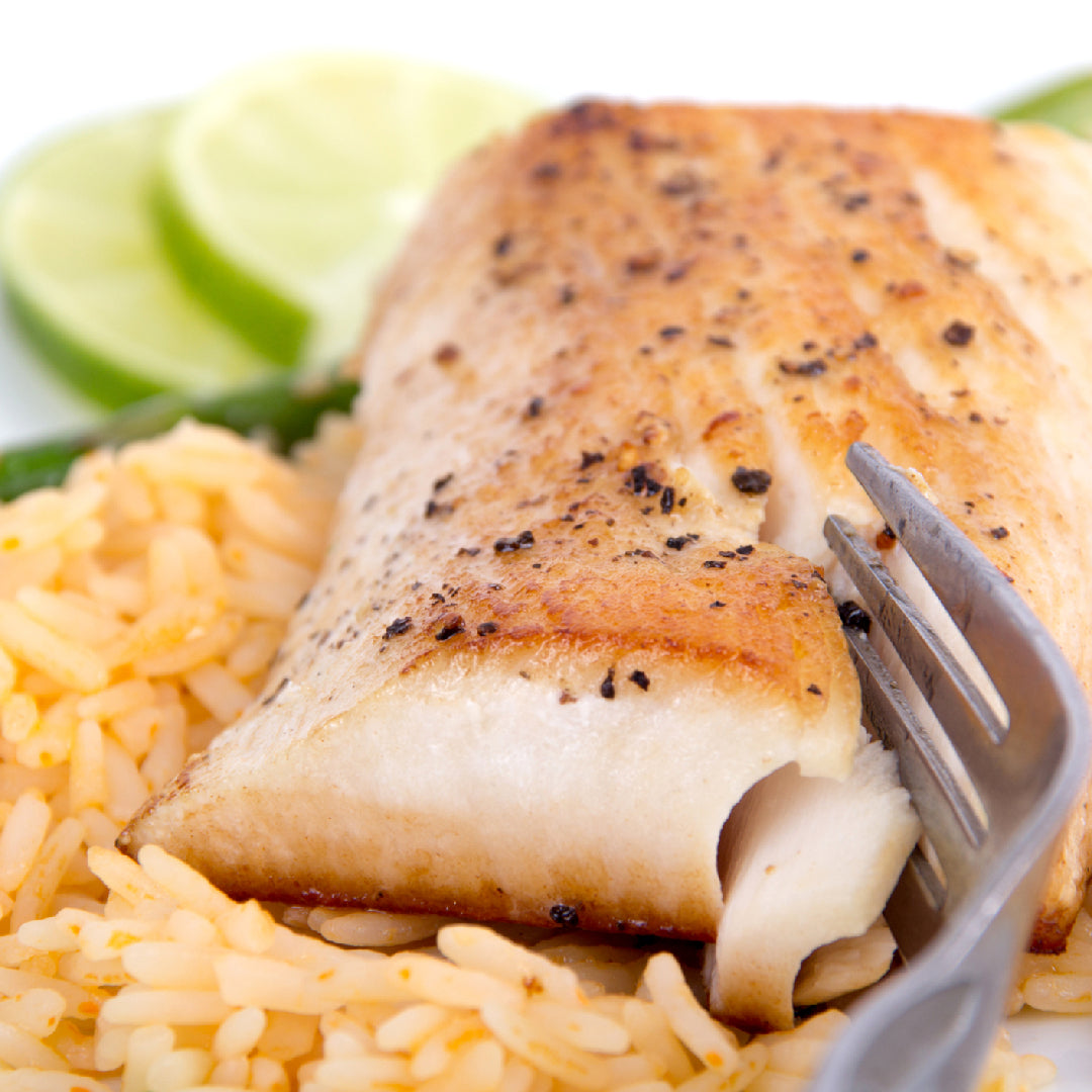 Grilled Pacific halibut fillet on a grill with lemon and fresh herbs