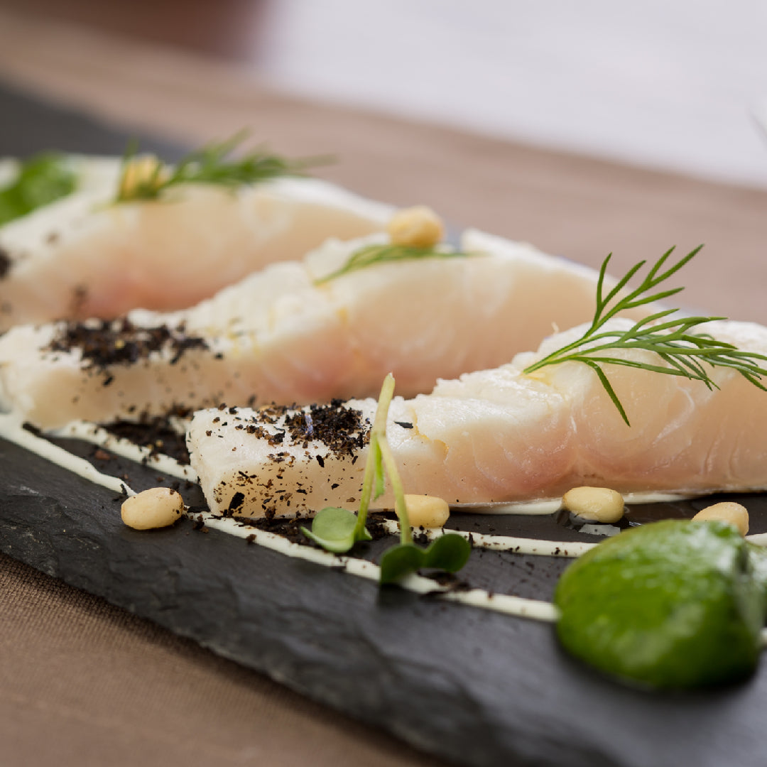 Side-by-side comparison of wild-caught Pacific halibut fillet and Atlantic salmon fillet on a wooden board