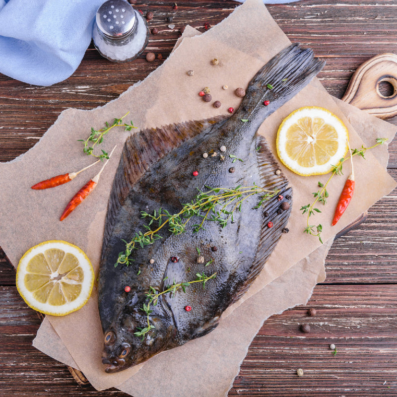 Whole flatfish on parchment with lemon slices, herbs, and chili peppers