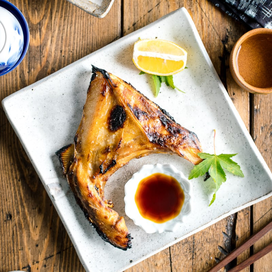 Hamachi fish fried rice in a wok garnished with sliced green onions, sesame seeds, and lime wedges on a dark wooden surface