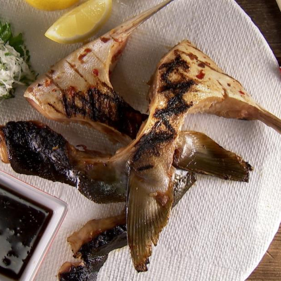Golden crispy Hamachi fish and chips served on parchment paper with lemon wedges, tartar sauce, and fresh parsley garnish