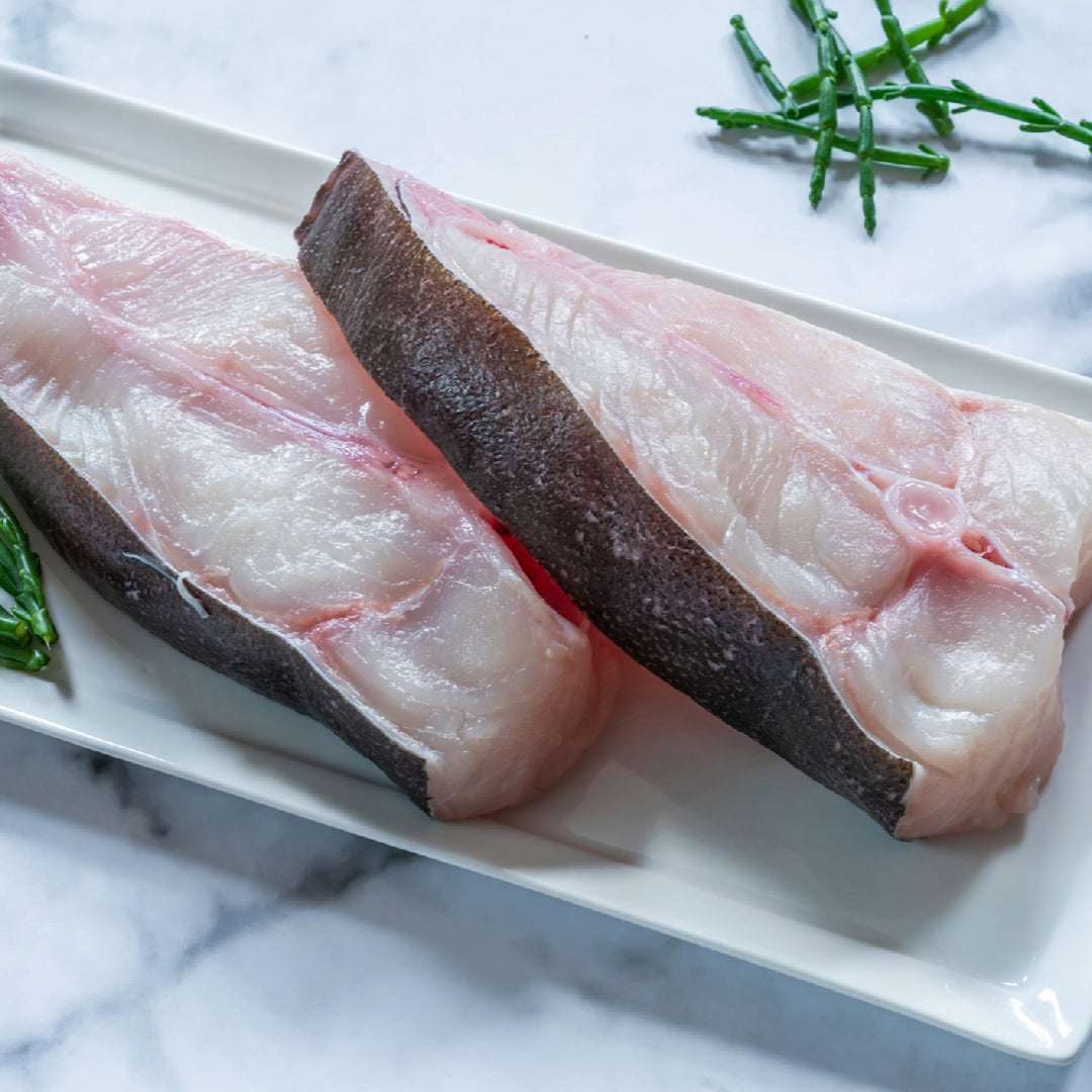 Fresh Pacific halibut fillet on ice next to a whole halibut, showing the white flesh and firm texture