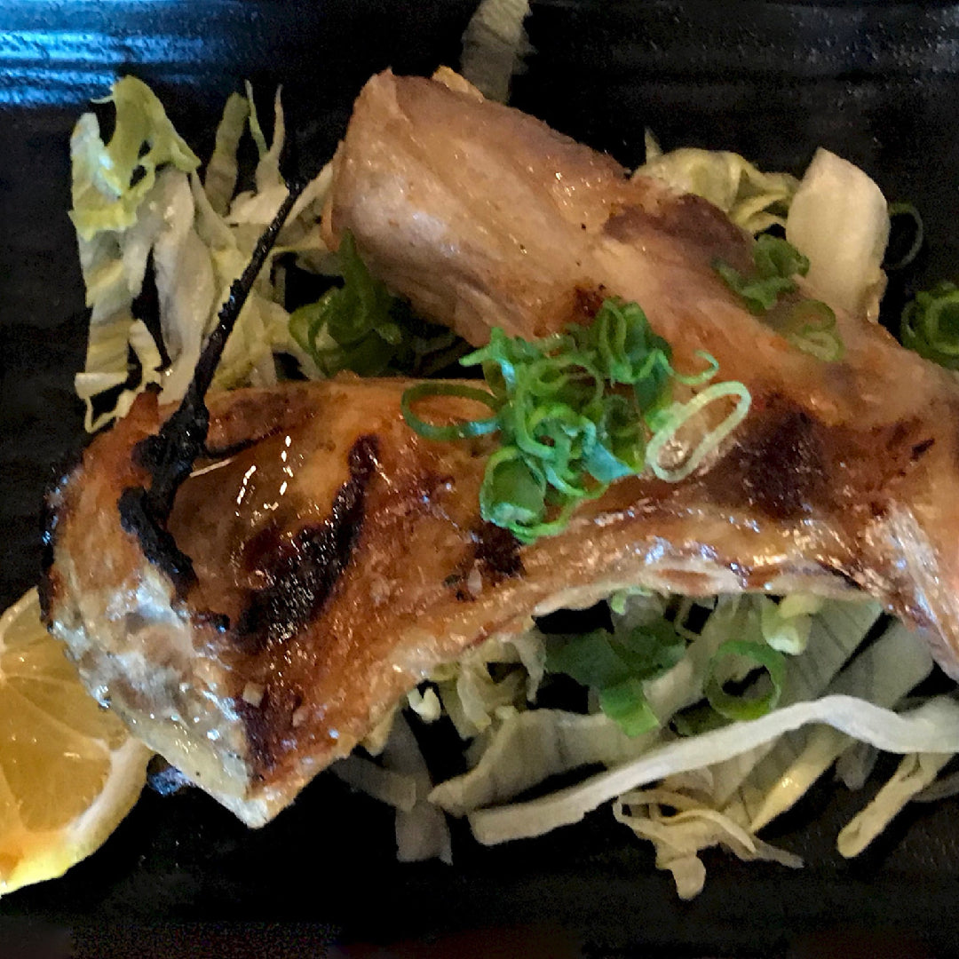 Fresh Hamachi yellowtail fillet on a hot grill with char marks, surrounded by lemon slices and fresh herbs