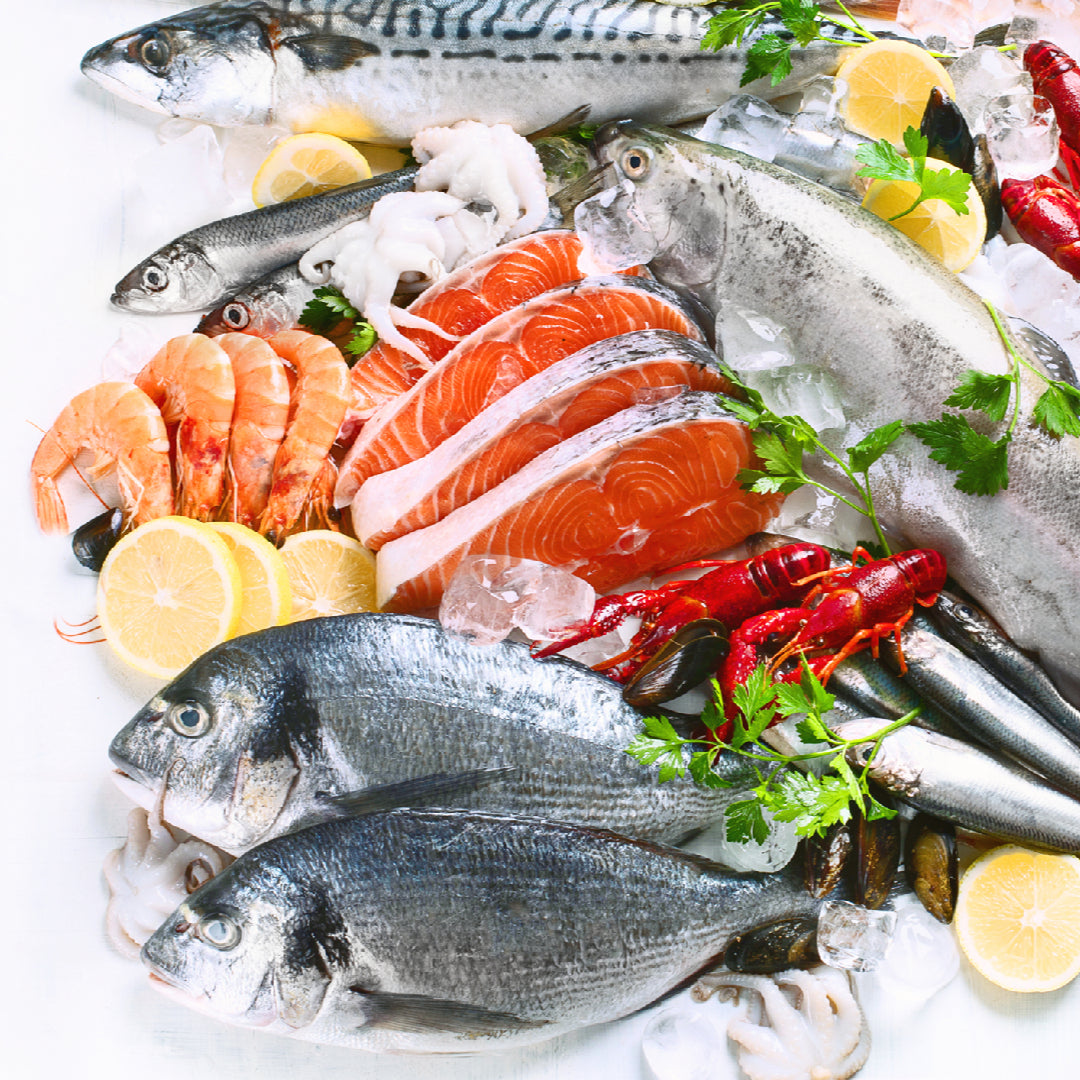 Five healthy seafood choices arranged on ice: wild salmon fillet, sardines, king crab legs, mussels, and caviar on a serving board