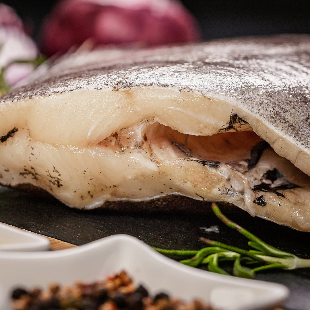 Close-up of a raw skin-on fish section with herbs and seasoning nearby