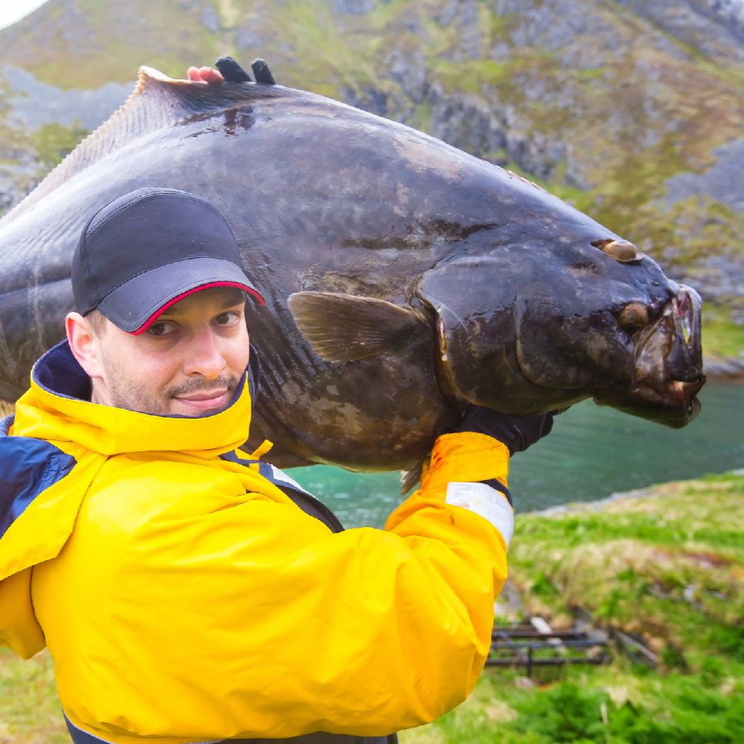 Angler holding a massive halibut on a fishing boat in Alaska with ocean in the background