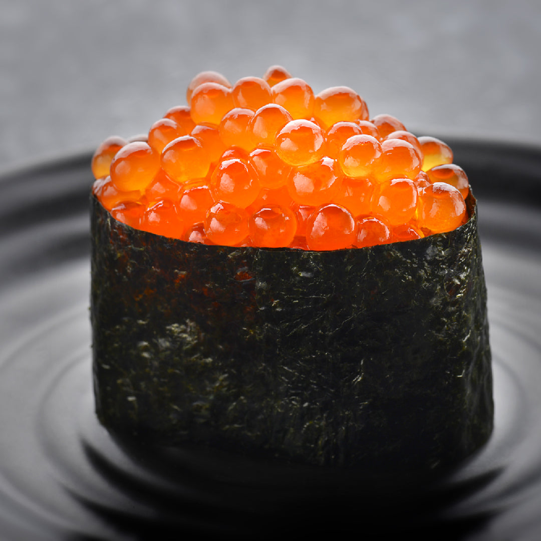 Ikura bibimbap in a stone bowl with vibrant orange salmon roe in the center, surrounded by sautéed vegetables, a fried egg, and gochujang sauce