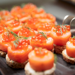 Close-up of bright orange salmon roe delicately placed atop fresh salmon sushi rolls, garnished with a sprinkle of green chives