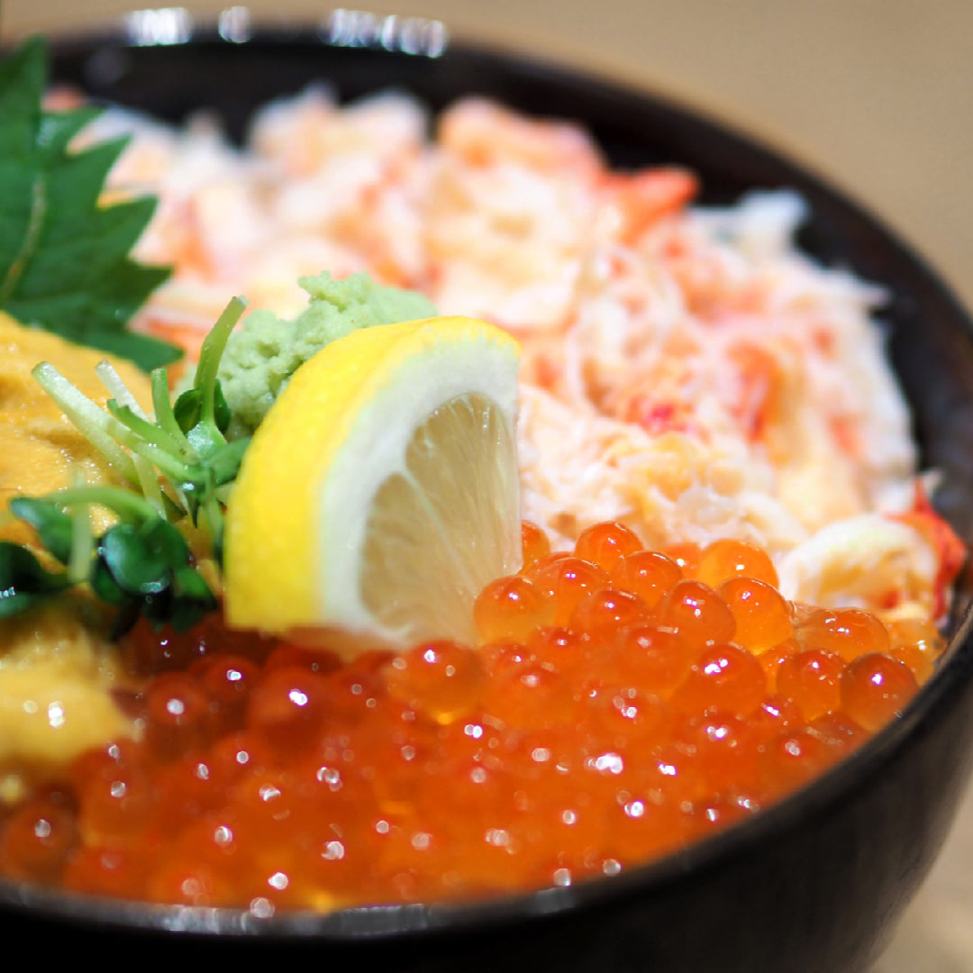 A photo of a sushi bowl topped with bright orange ikura and green onions.