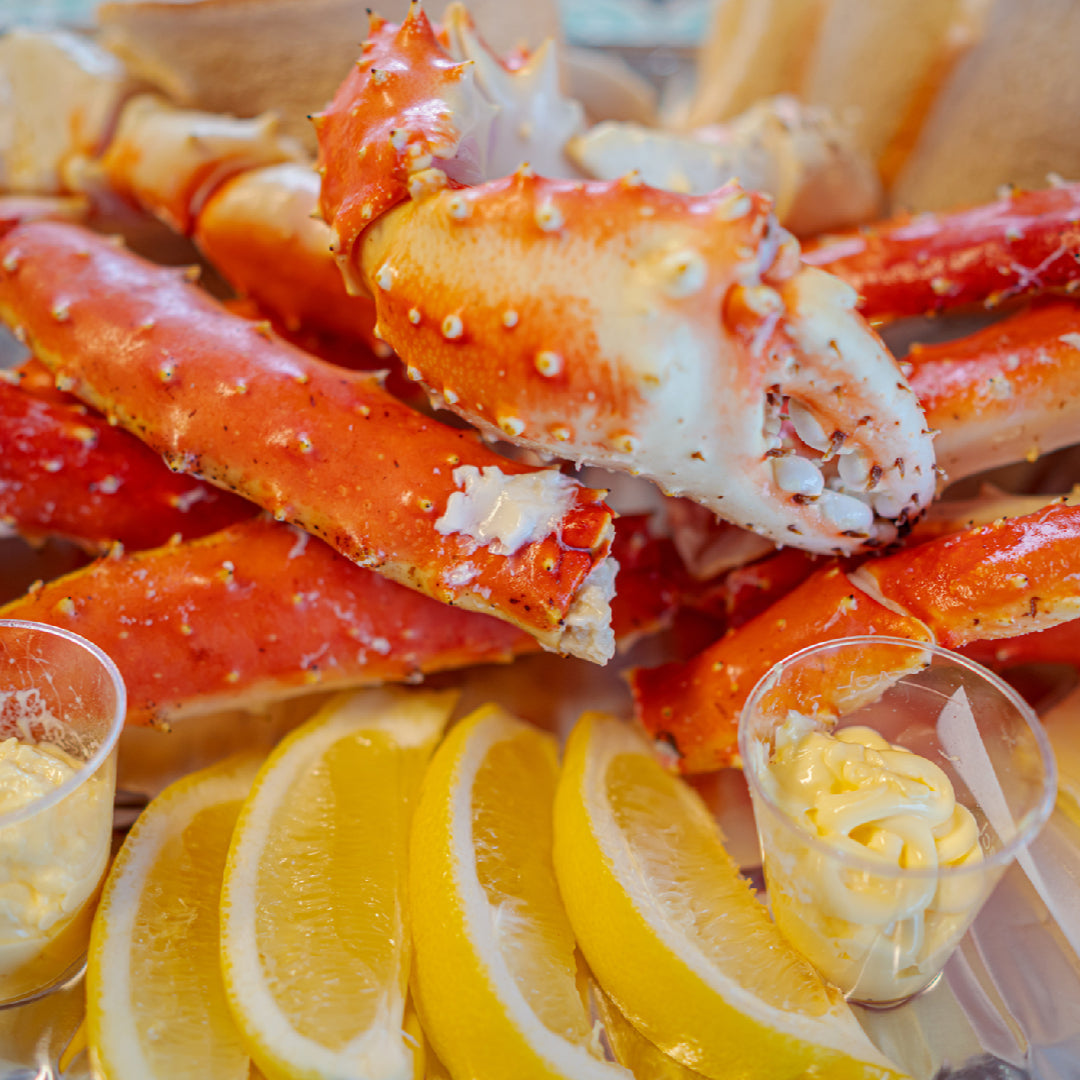 Baked king crab legs on a foil-lined baking sheet brushed with garlic butter sauce, garnished with fresh parsley and lemon wedges