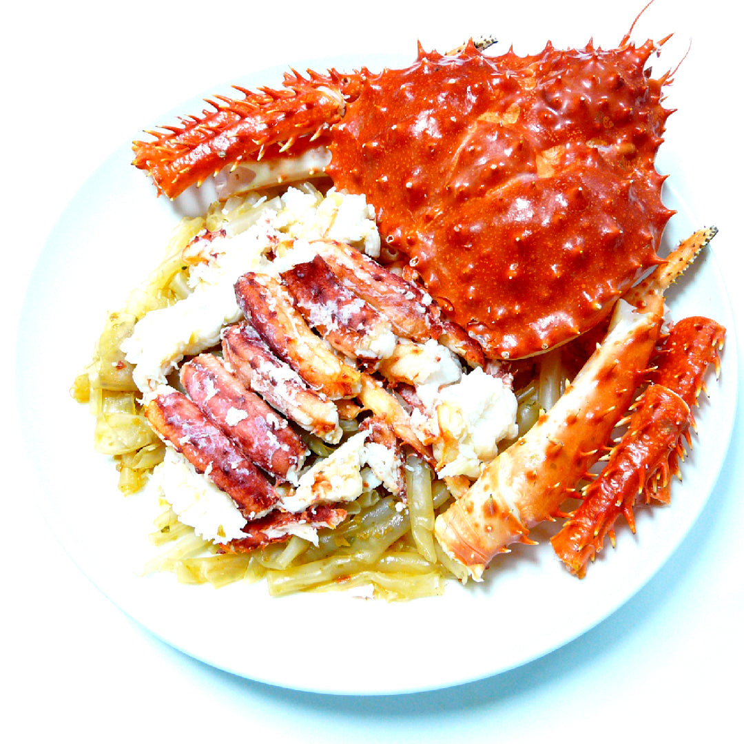 Freshly cooked Alaskan red king crab legs on a platter with drawn butter and lemon — the result of a dangerous and labor-intensive journey from the icy Bering Sea to your plate