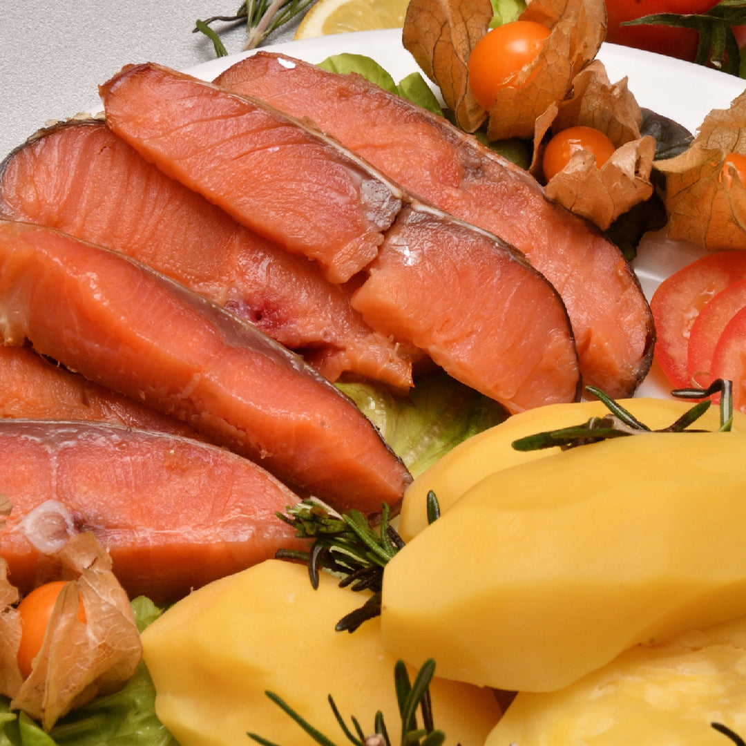 Chef filleting a large King Chinook salmon on a wooden cutting board with a sharp fillet knife, showing the bright orange-red flesh