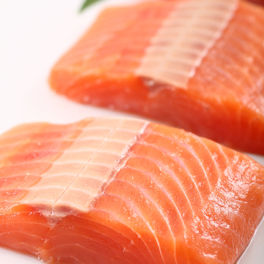 Fresh wild Alaskan King salmon fillet on a wooden board showing its deep orange marbling, with lemon and fresh herbs