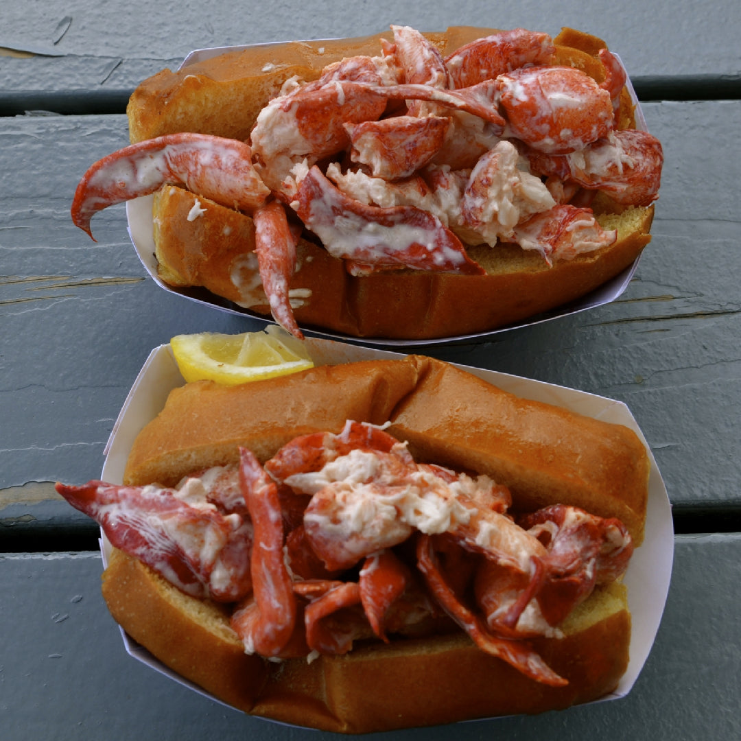 Hands using a seafood cracker to crack open a cooked lobster claw on a wooden board