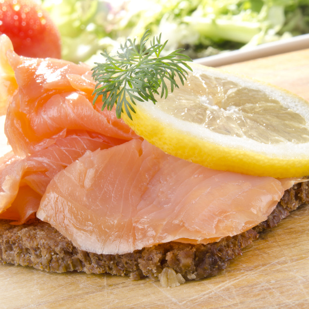 Thinly sliced Ora King Salmon gravlax on a wooden board with dill, capers, and lemon