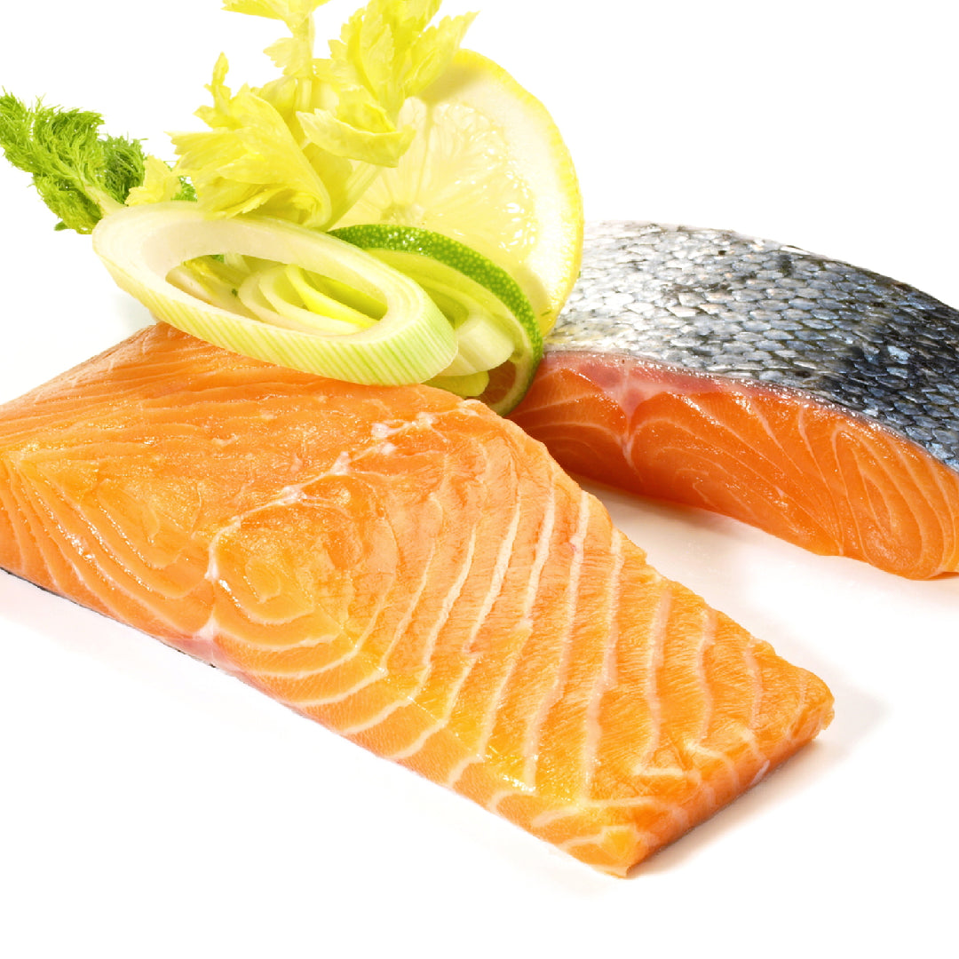 Ora King Salmon fillet grilling on a barbecue with char marks, garnished with lemon and herbs
