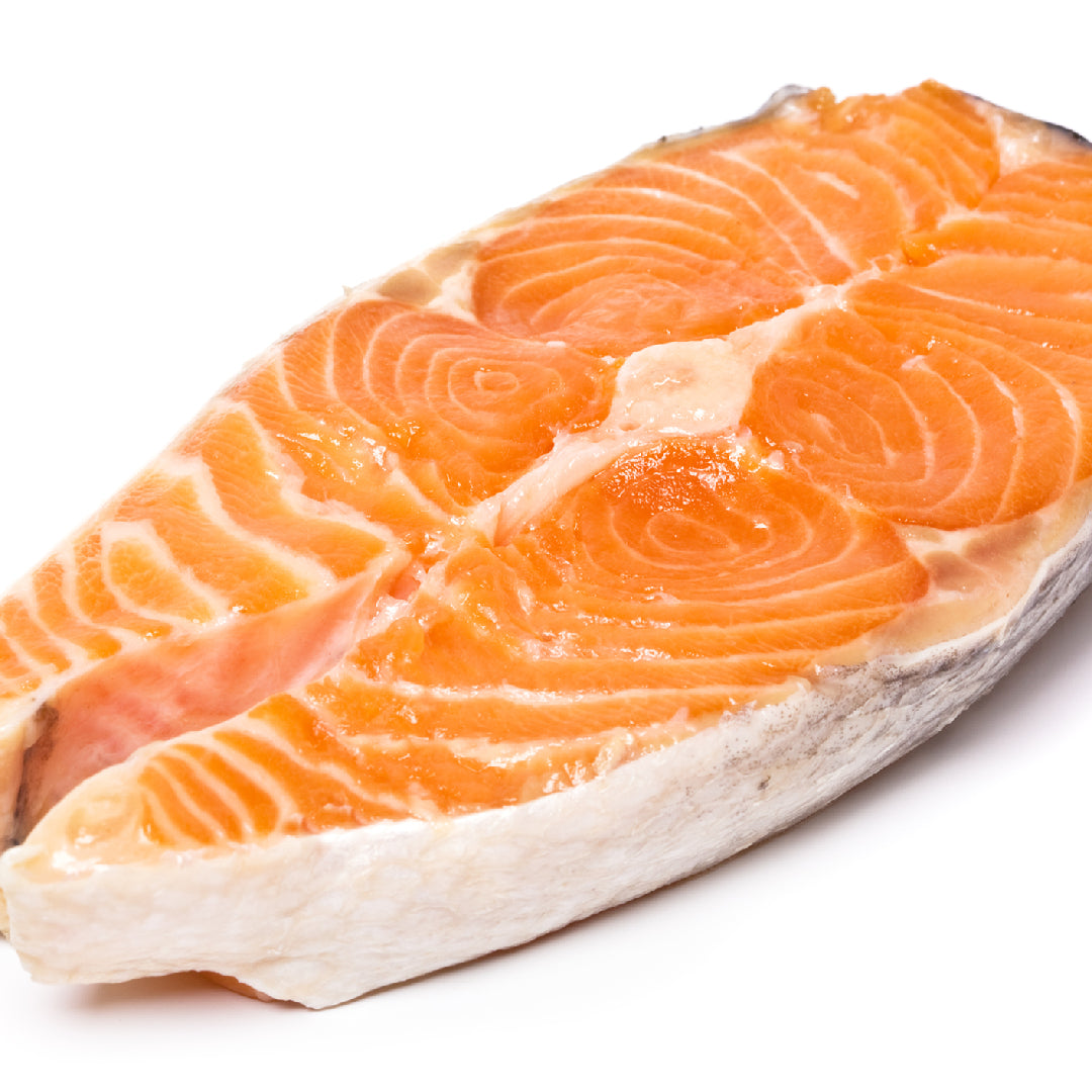 Ora King Salmon fillet on a grill with char marks and lemon slices, surrounded by smoke
