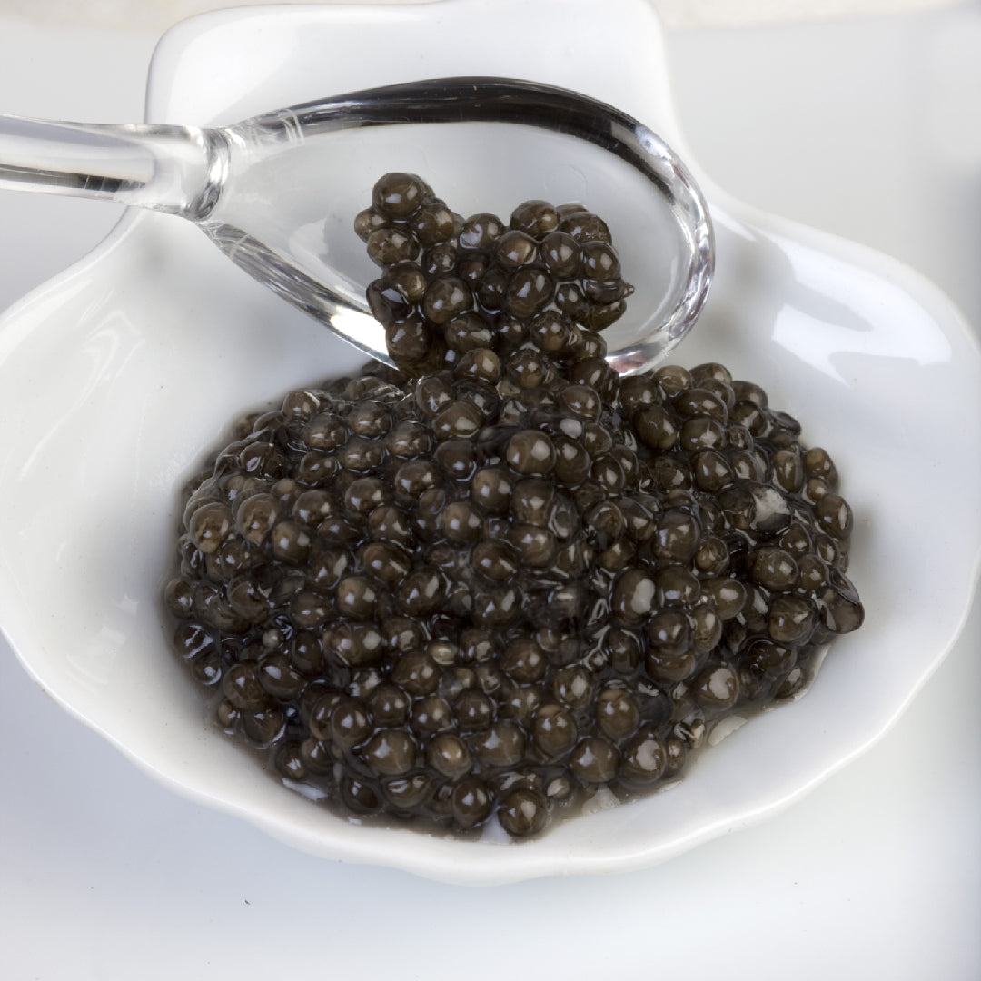 Ossetra caviar and shaved black truffle on a white plate with blinis and champagne in the background