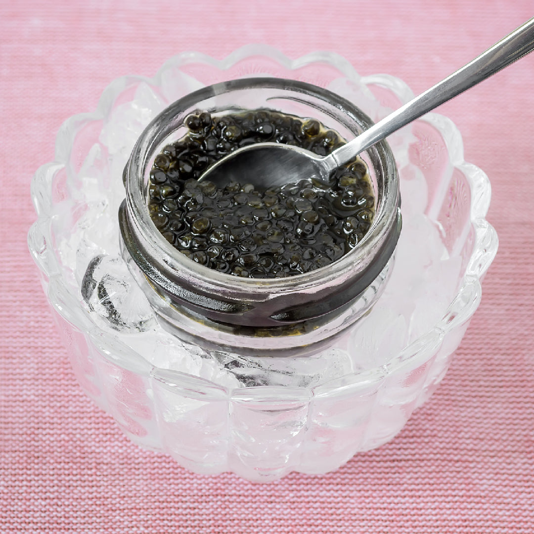 Creamy spaghetti topped with golden Ossetra caviar pearls and fresh herbs in a white bowl on a marble surface