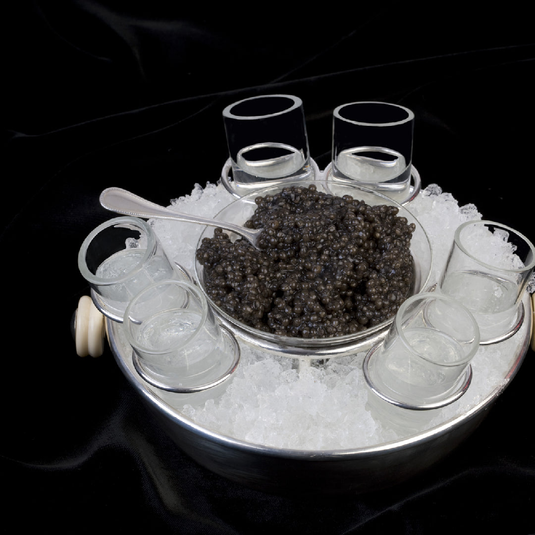Osetra caviar served in a mother-of-pearl spoon over crushed ice with blinis and crème fraîche on a marble surface