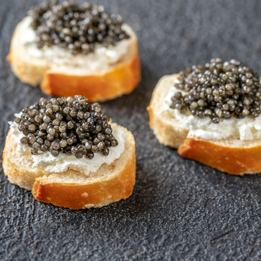 Close-up of Osetra caviar pearls ranging from golden to dark brown on a mother-of-pearl spoon, served on crushed ice with blini and crème fraîche