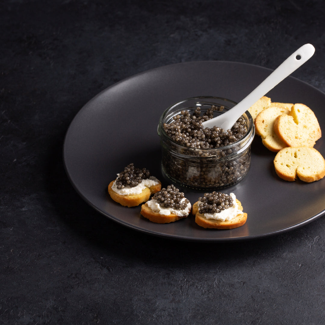Chilled Osetra caviar tin served alongside a flute of champagne and blinis on a white linen tablecloth