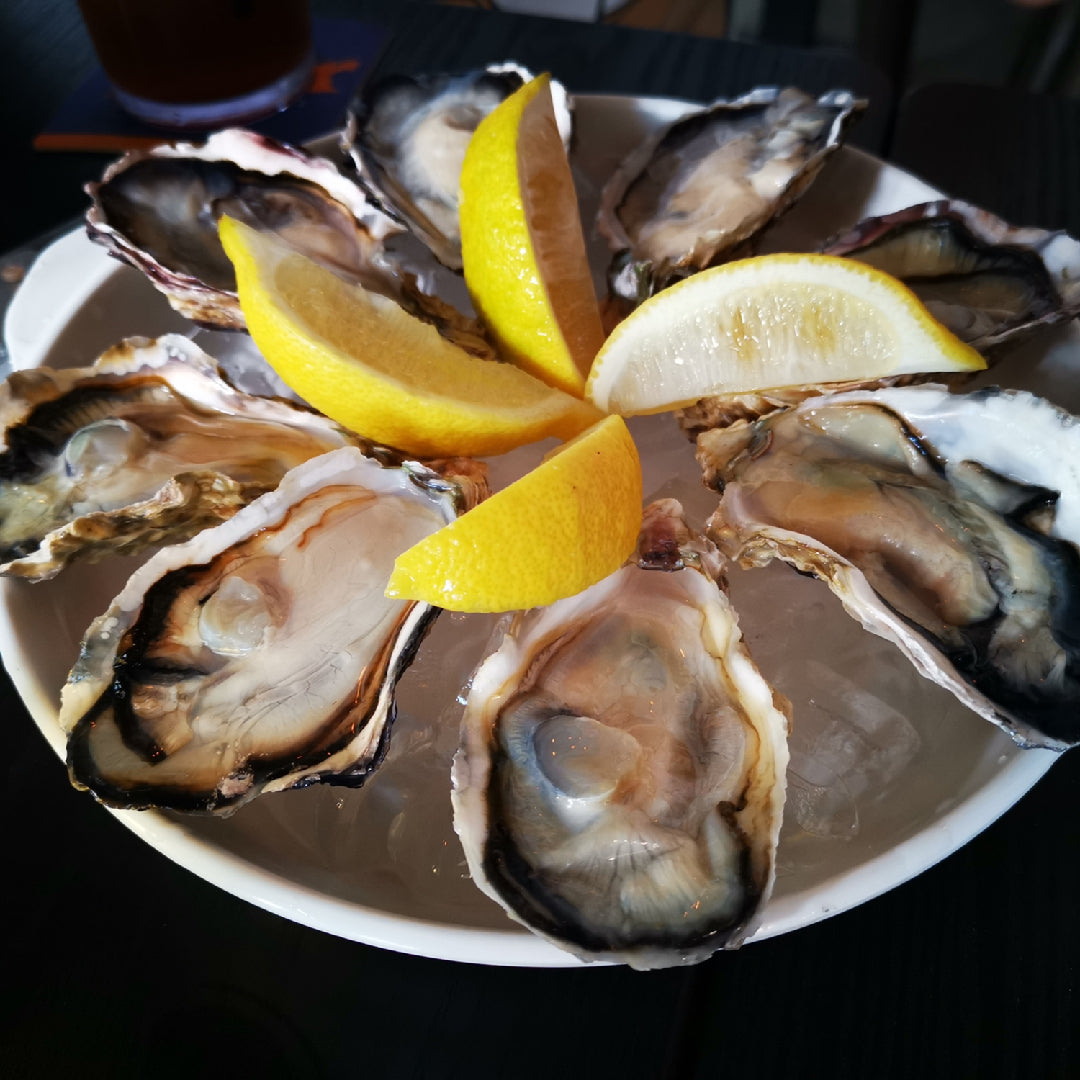 Fresh oysters on a half shell arranged on ice at an oyster bar with mignonette sauce and lemon wedges
