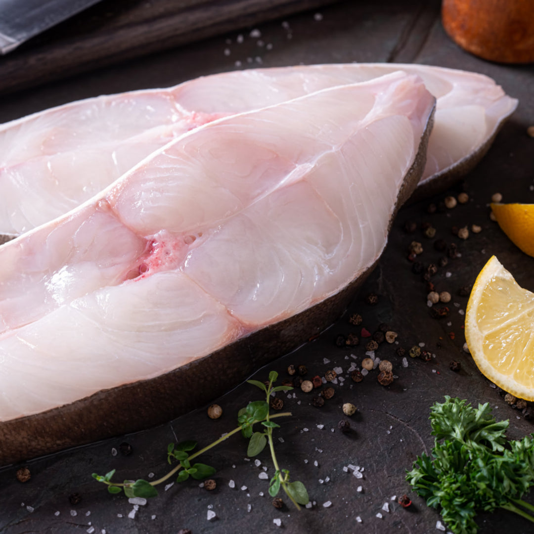 Pan-seared Pacific halibut fillet with a golden crust in a cast-iron skillet — showing the correct sear color and the thick, white flesh of wild-caught Pacific halibut
