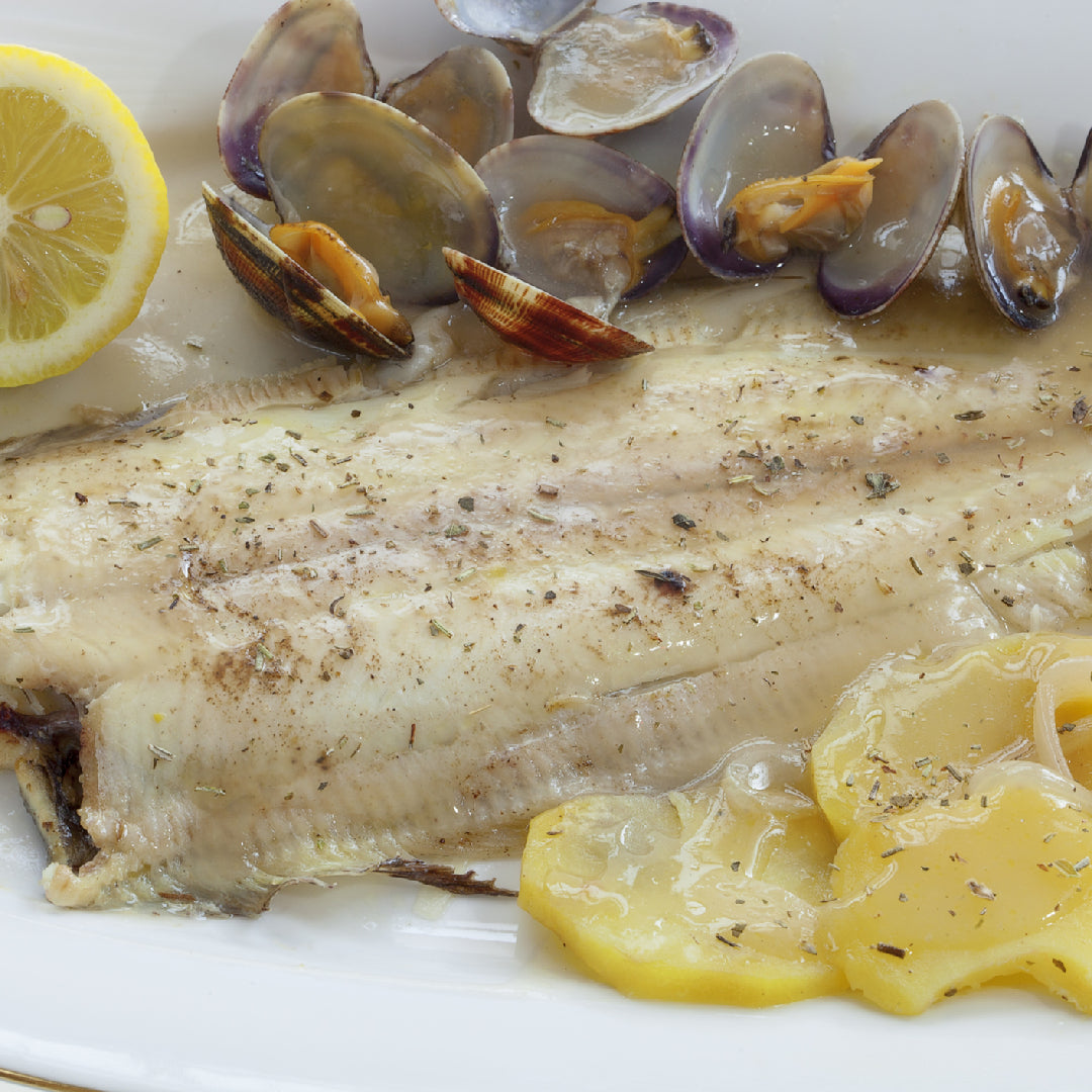 Multiple Petrale Sole fillets baked on a large sheet pan with lemon slices, rosemary, and thyme, ready to serve at a dinner party