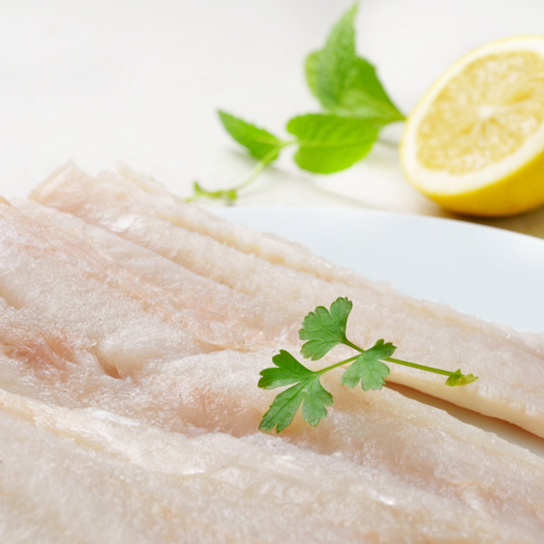Fresh Alaskan pollock fillets on a wooden board with lemon, herbs, and a fishing net in the background