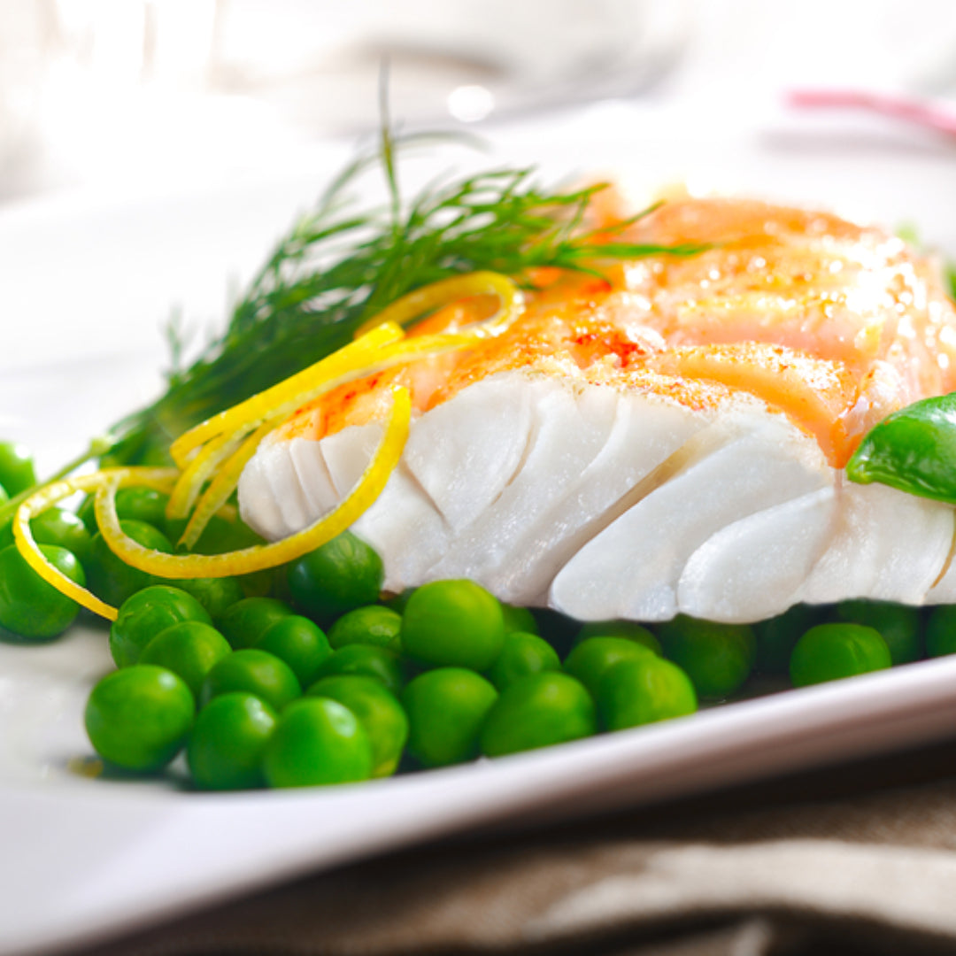 Fresh Alaskan pollock fillets on a cutting board with lemon and herbs