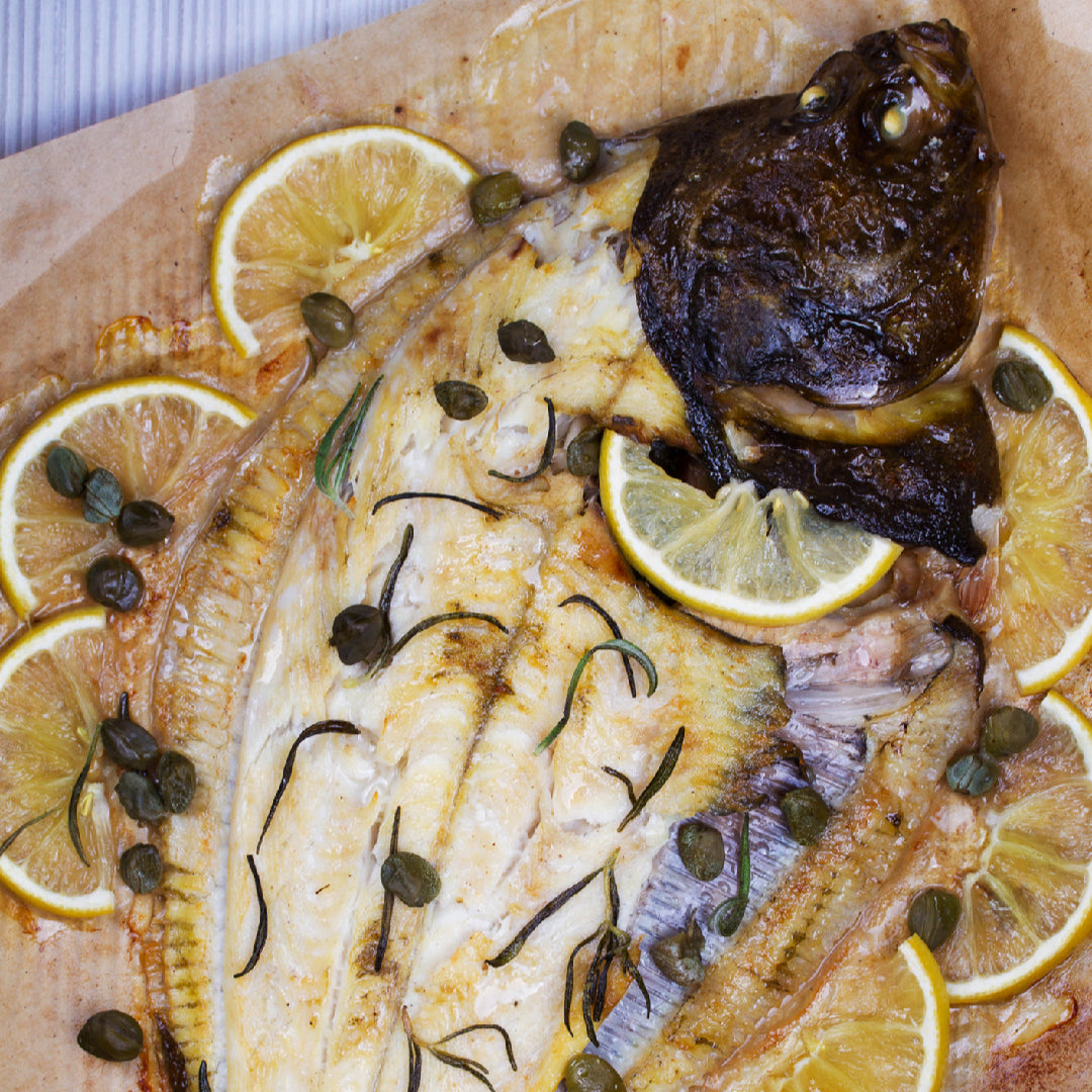 Grilled Petrale Sole fillets with lemon slices and fresh herbs (parsley, thyme, dill) on a grill – a light, healthy California seafood dish showcasing the mild sweet flavor and firm delicate texture of this premium Pacific flatfish