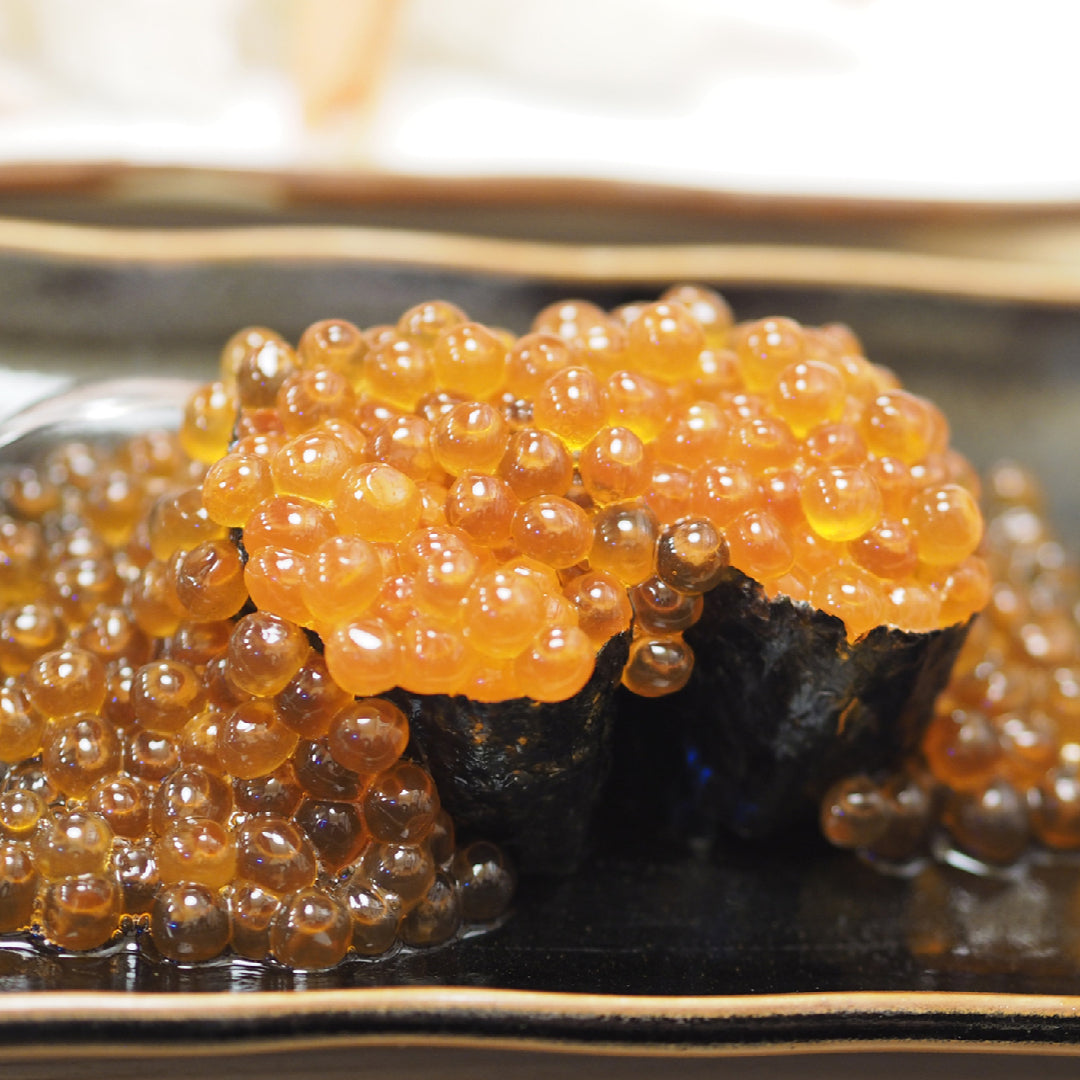 Grilled yakitori skewers of chicken and vegetables on a serving plate, topped with vibrant orange salmon roe, sliced green onions, and toasted sesame seeds