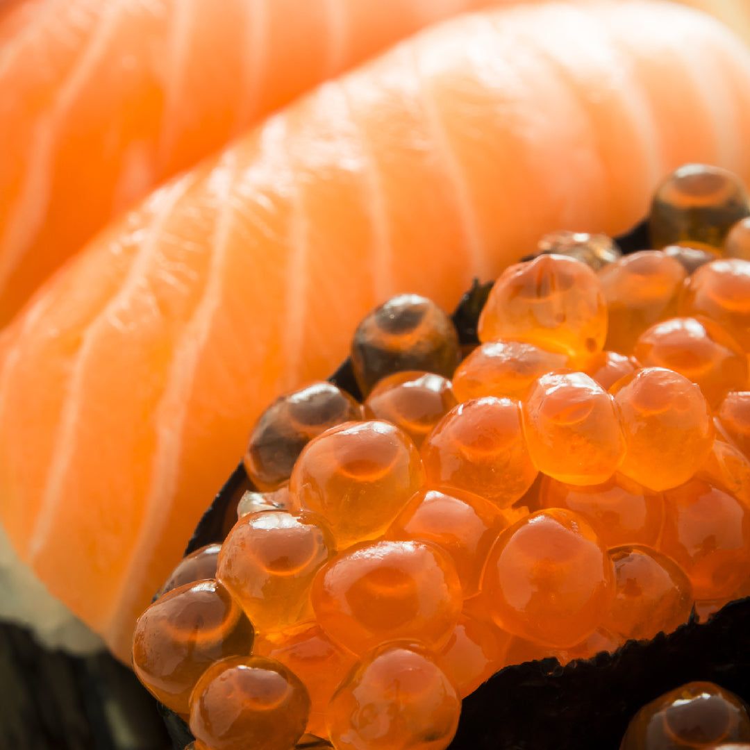 Ikura sashimi served in a small ceramic dish: vibrant orange salmon roe pearls garnished with shiso leaf, wasabi, and a light drizzle of soy sauce