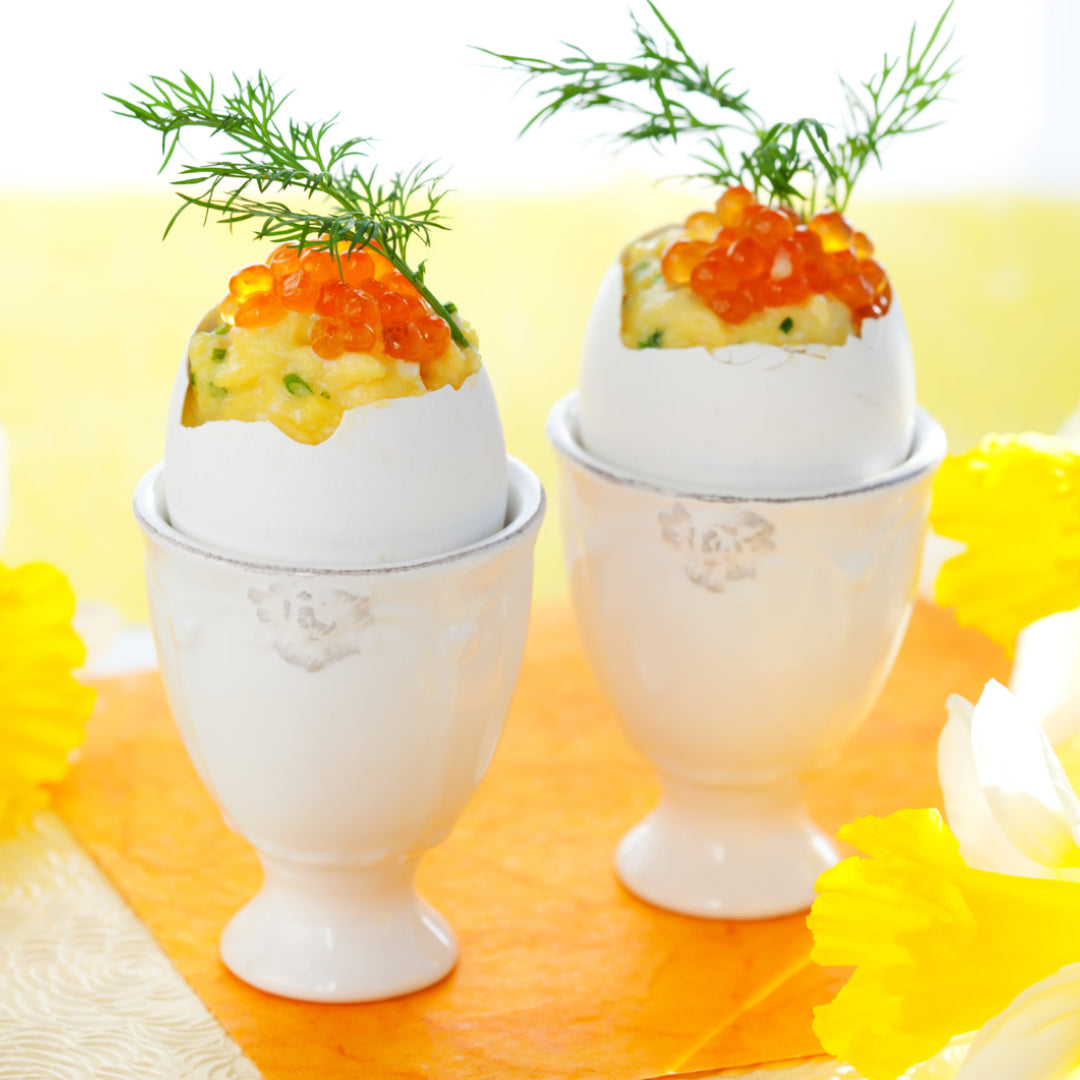 Creamy French-style scrambled eggs topped with bright orange salmon caviar and fresh chives, served in a white bowl with toasted brioche on the side
