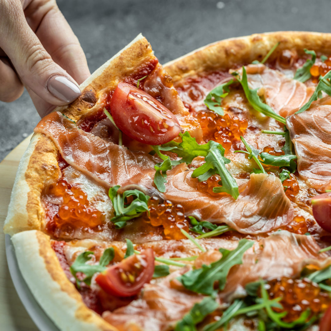 Gourmet red caviar pizza on a thin crispy crust with crème fraîche base, topped with bright orange salmon roe, smoked salmon, capers, and fresh dill, served on a wooden board