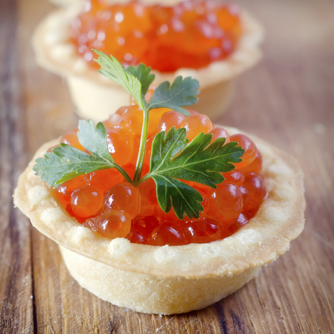 Salmon roe being gently sautéed in butter in a non-stick pan, with scrambled eggs and fresh chives on a wooden board nearby