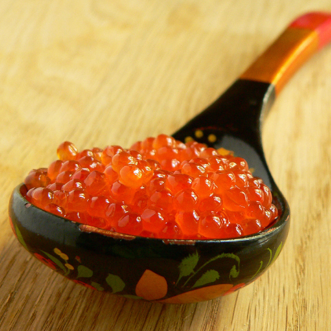 Salmon roe served on blinis with crème fraîche alongside a glass of champagne and chilled vodka on an elegant table setting