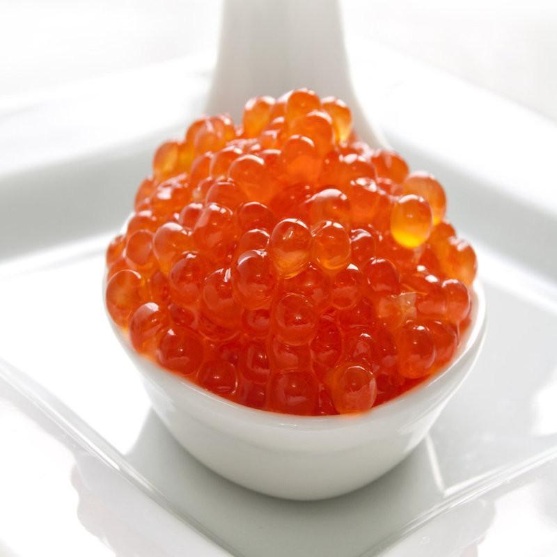 Golden-red chum salmon caviar pearls served in a small dish with blinis and crème fraîche
