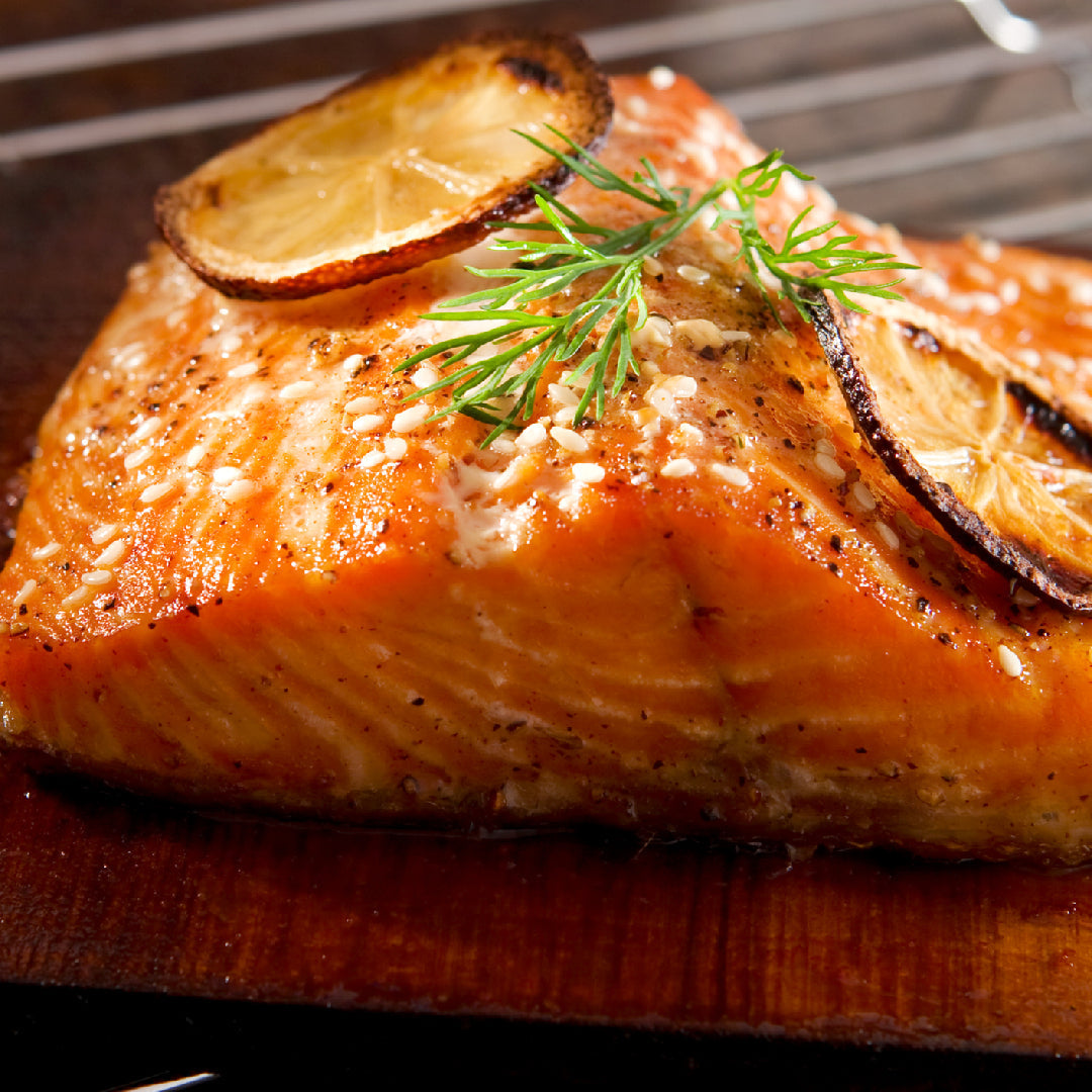 Grilled salmon platter with lemon butter sauce, fresh herbs, and grilled vegetables on a wooden serving board