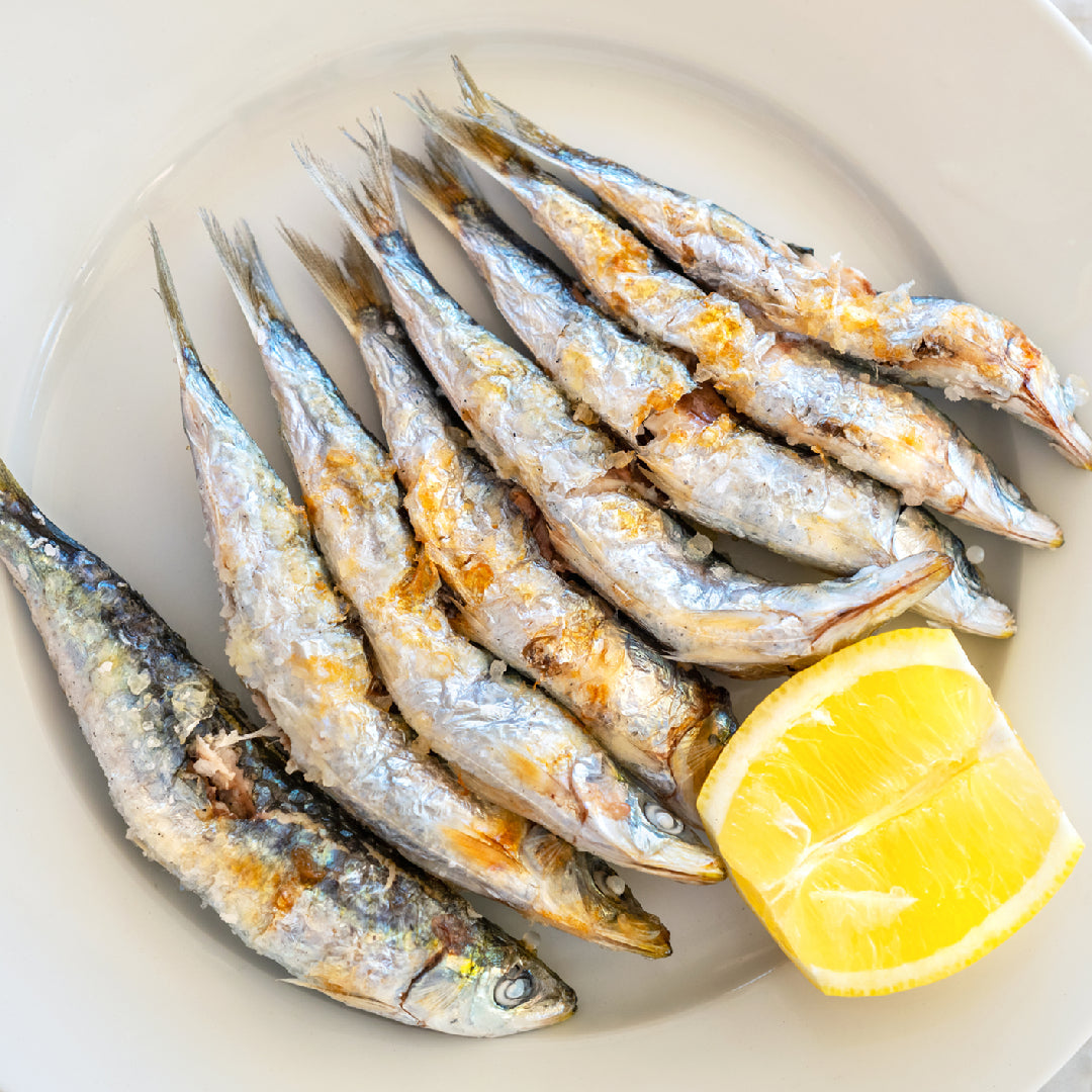 Golden sardine focaccia topped with cherry tomatoes, red onion, fresh rosemary, and olive oil drizzle on a wooden cutting board