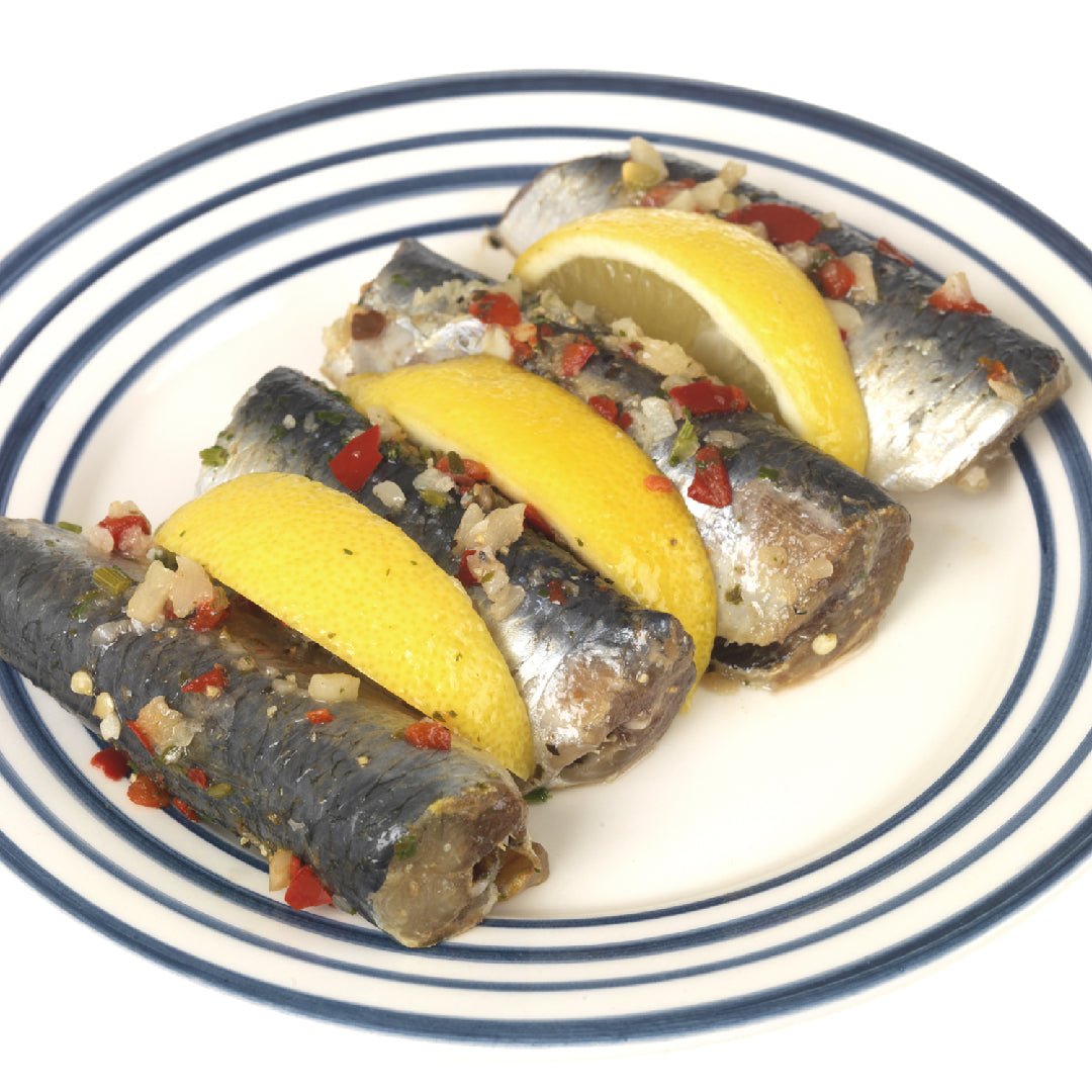 Sardine snacks on whole-grain crackers with mashed avocado, capers, fresh dill, and lemon arranged on a wooden serving board