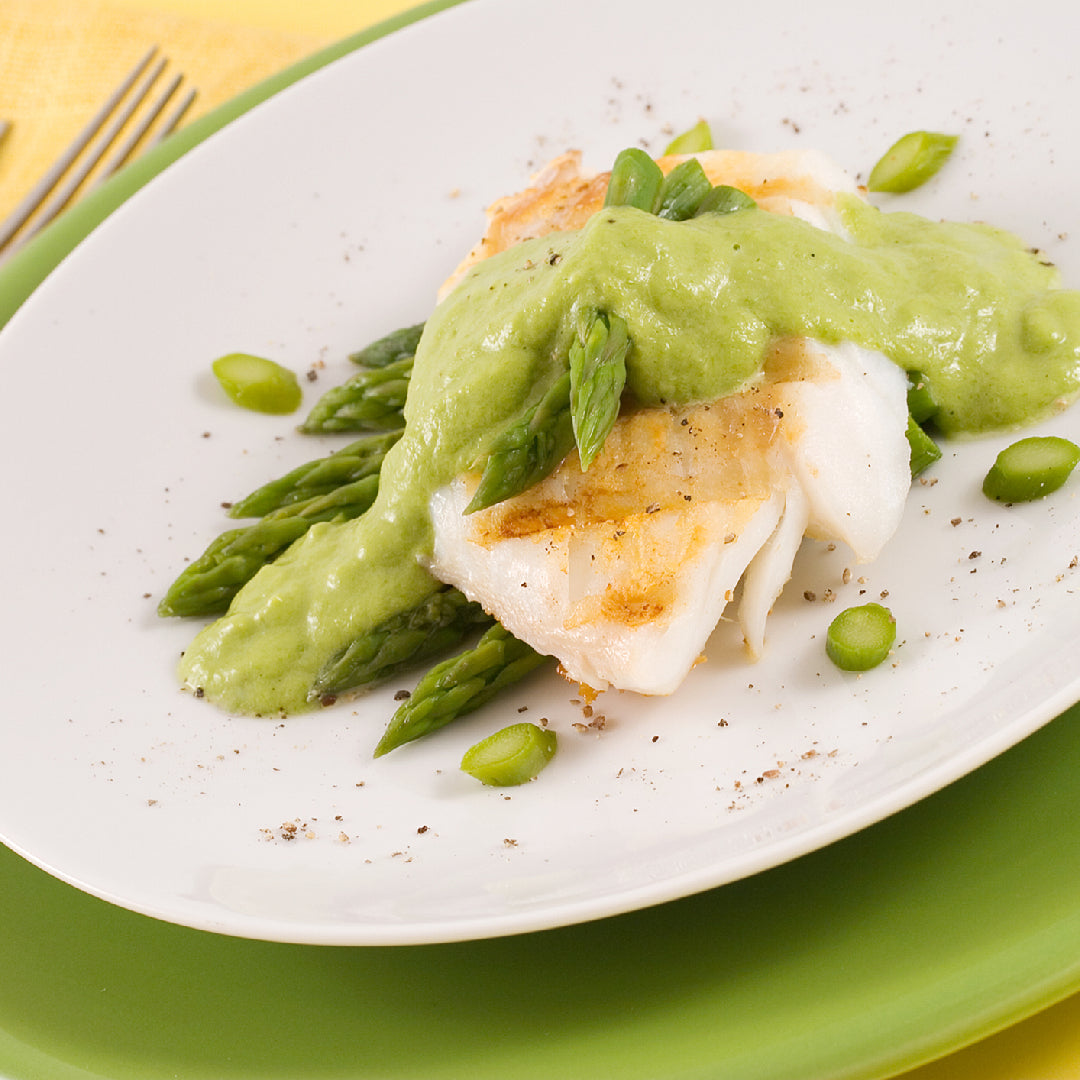 White fish with green sauce and asparagus on a white plate.