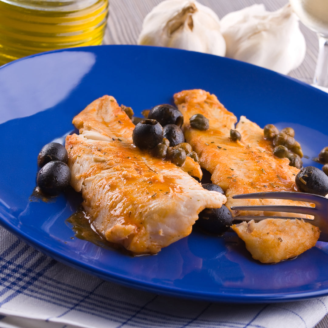 Sablefish fillet being pan-seared in a cast iron skillet with lemon and herbs