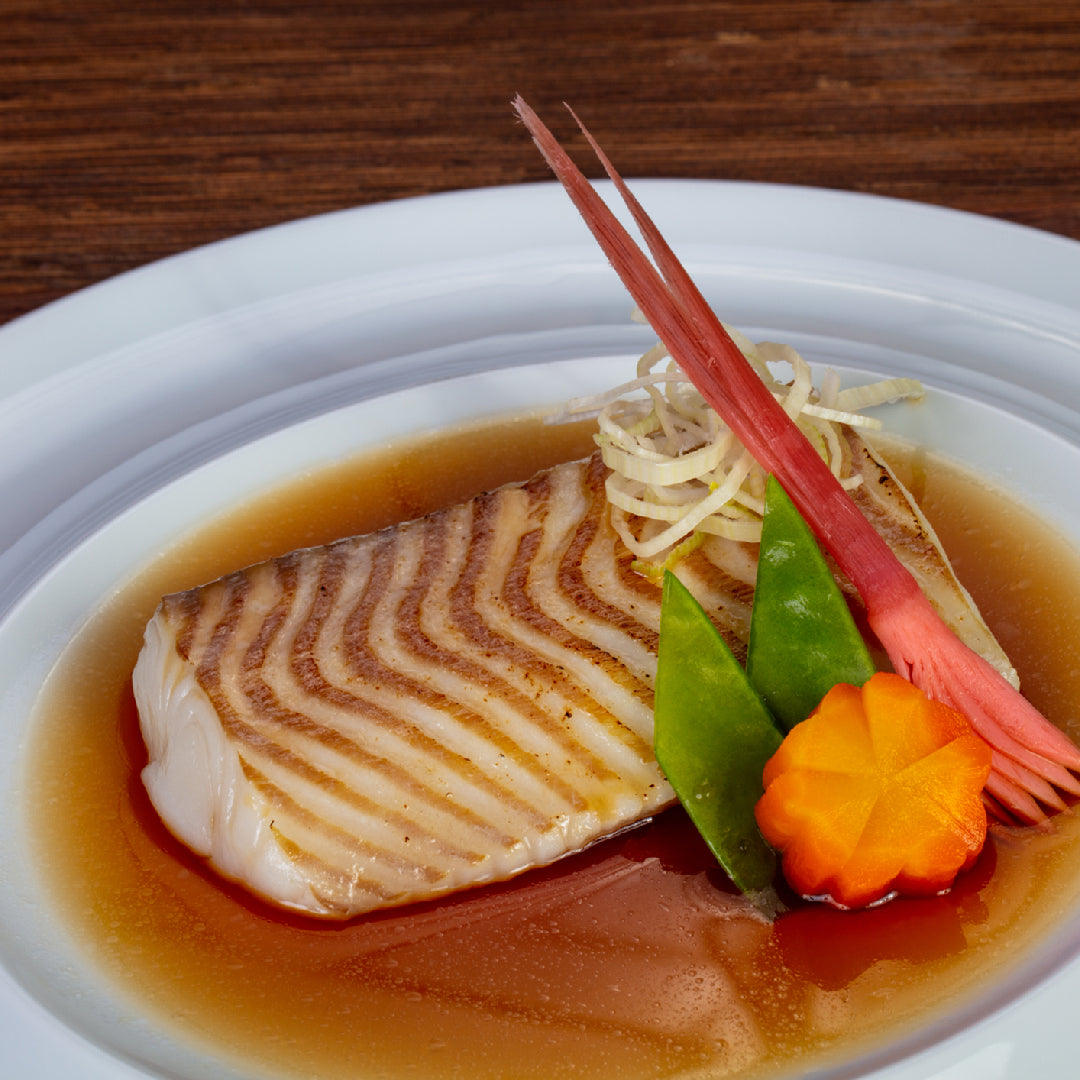 Cooked fish in a brown sauce with vegetables on a white plate.
