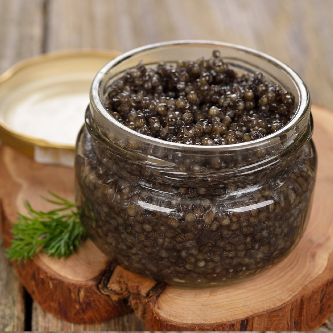 Open tin of premium sturgeon caviar with glistening black pearls resting on crushed ice, served with a mother-of-pearl spoon and blinis on an elegant marble surface