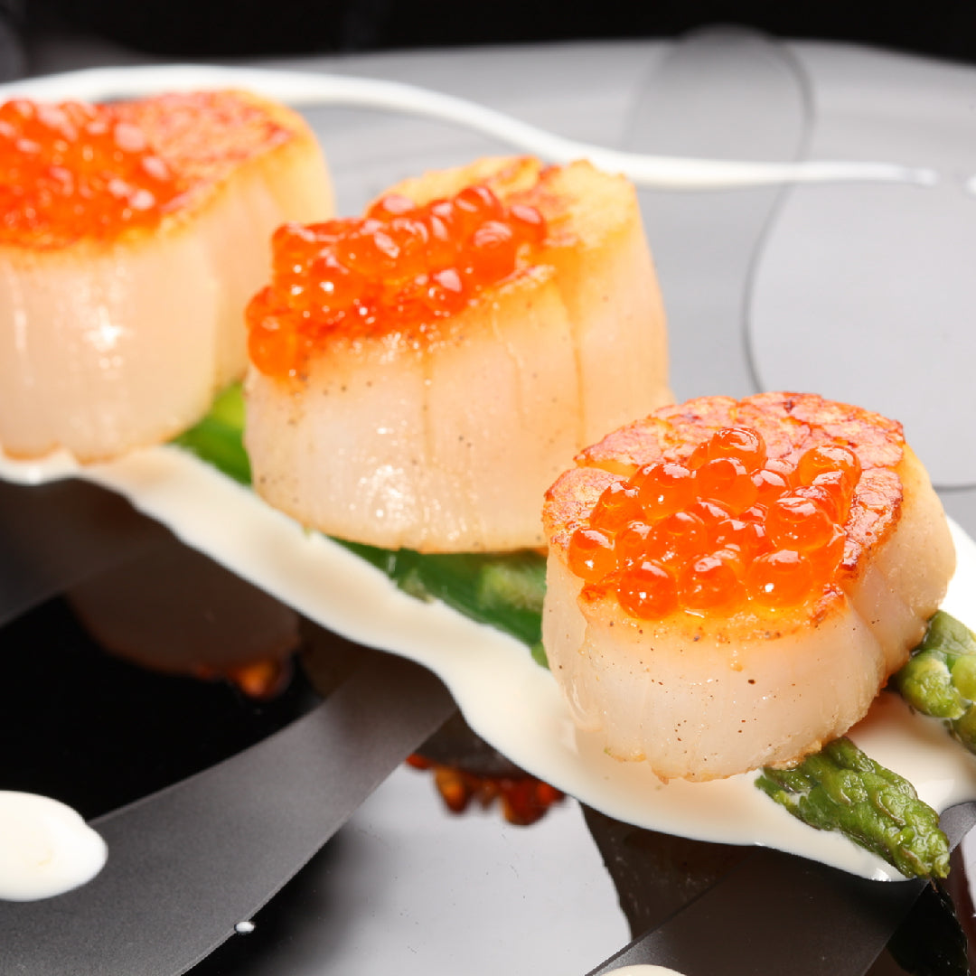 Fresh diver scallops with golden sear in a cast iron pan garnished with herbs and lemon