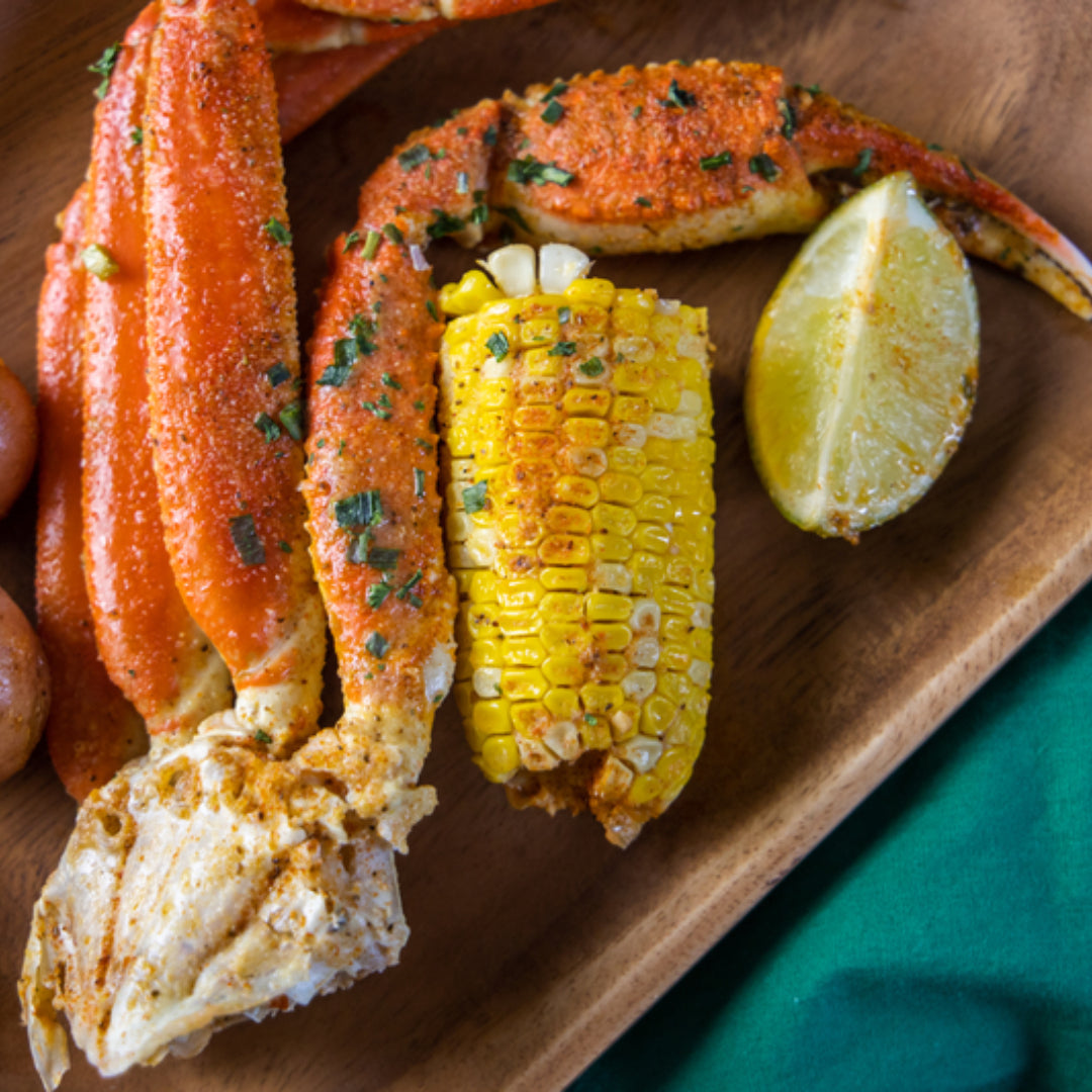 Assorted side dishes for crab legs including roasted potatoes, grilled asparagus, corn on the cob, coleslaw, and cornbread on a rustic table