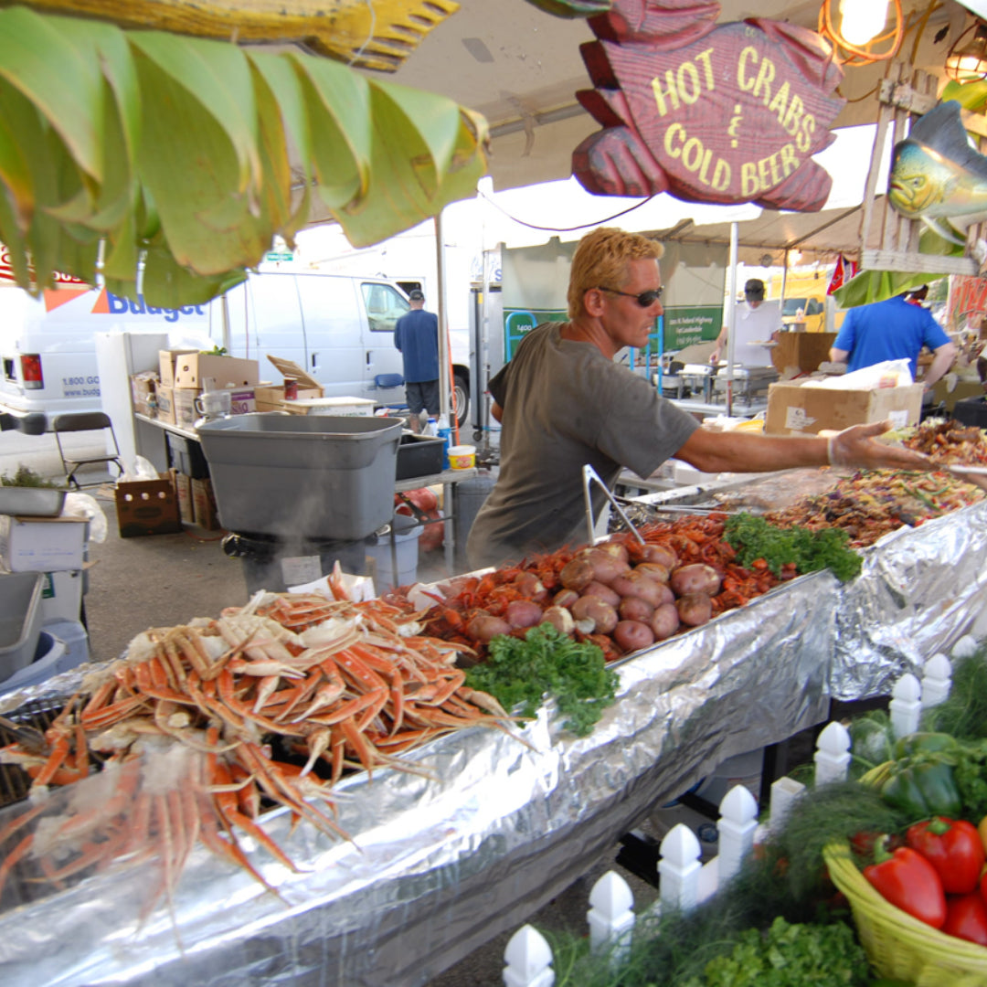 Crowds gathered at an outdoor crab festival with steamed blue crabs, Old Bay seasoning, and craft beer on picnic tables by the waterfront
