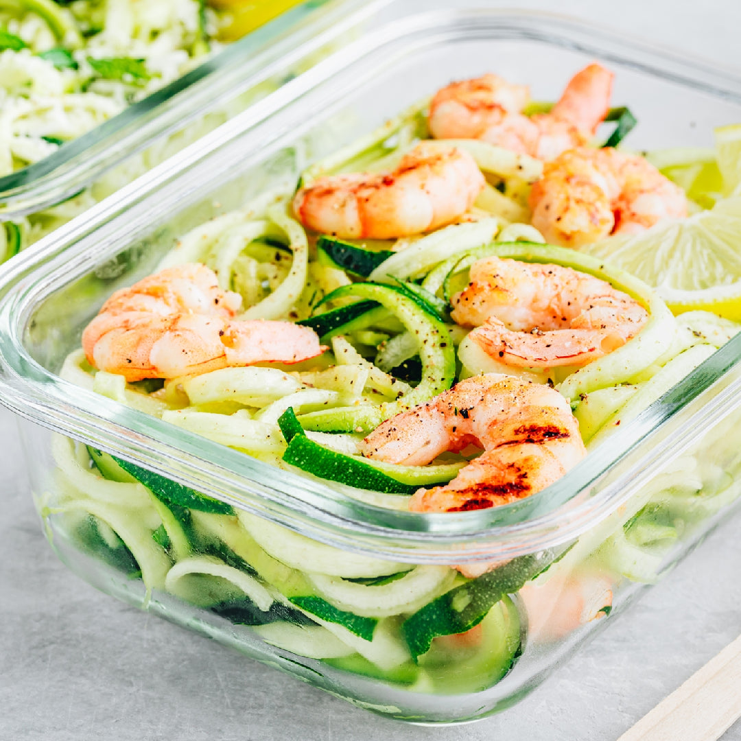 Five seafood meal prep containers arranged on a kitchen counter, showing baked salmon, shrimp quinoa salad, tuna avocado, stir-fry, and sablefish with rice